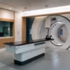 Empty carbon ion radiotherapy treatment room with a circular gantry and aligned patient table.